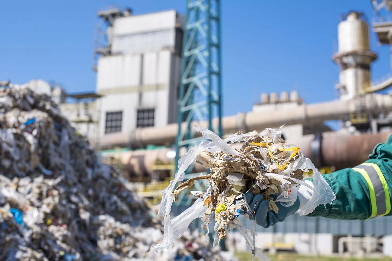 Hand mit Handschuhen hält Recyclingmaterial vor einer Anlage